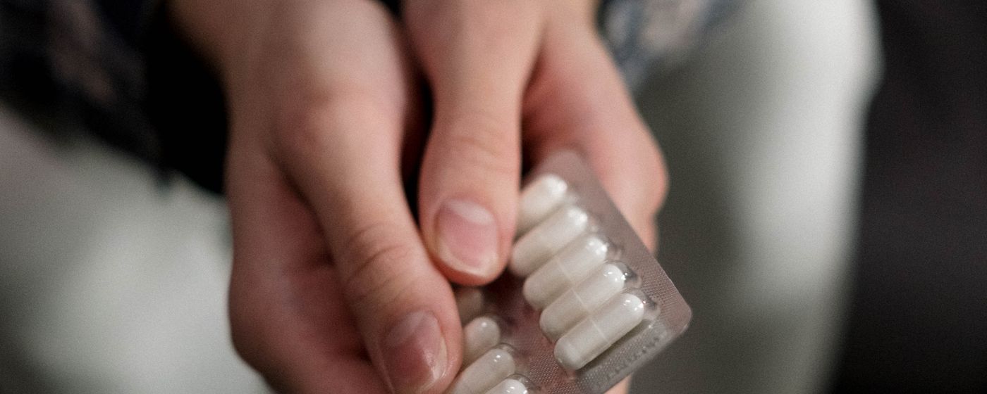 Hands holding a blister pack of white capsules