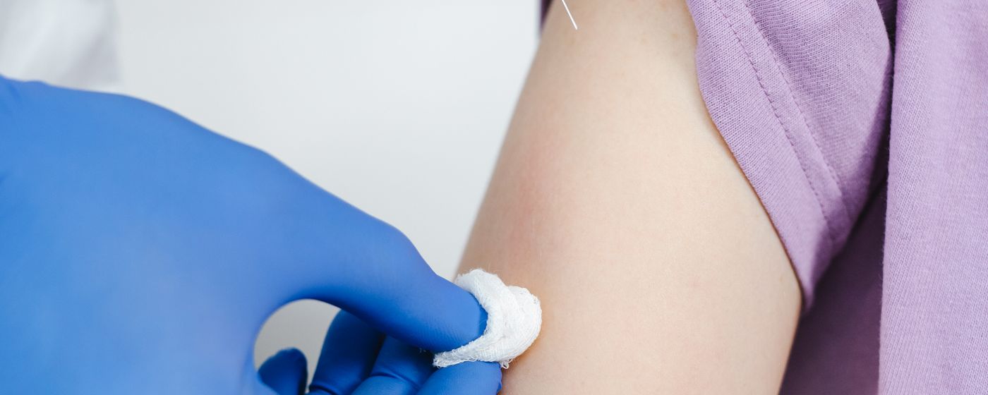 A gloved clinician preparing a patient's upper arm for a vaccination