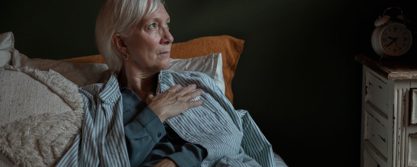 A woman resting in bed at night with her hand on her chest