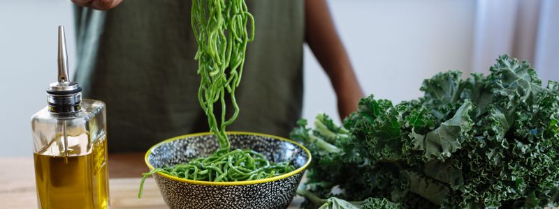 A bottle of olive oil beside fresh kale and a bowl of greens