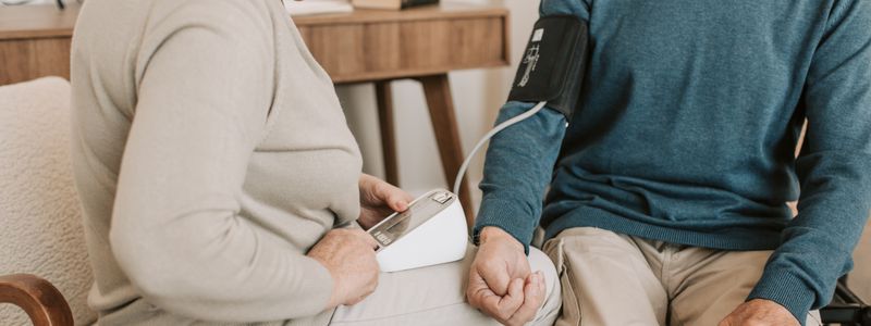 A clinician taking an older man's blood pressure at home