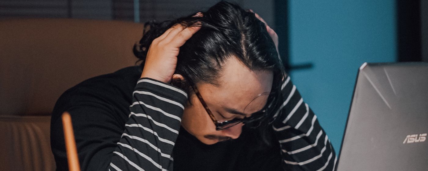 An overwhelmed man working late at a laptop with his hands in his hair