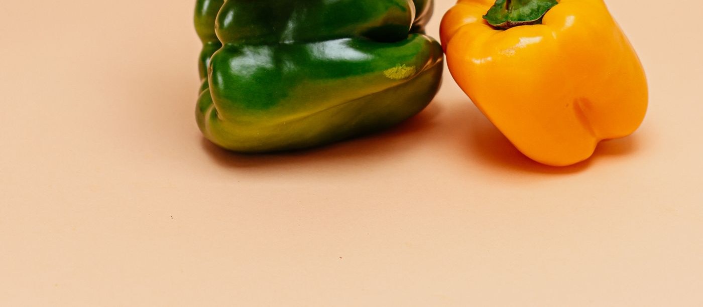 Red, green and yellow bell peppers stacked on a plain background