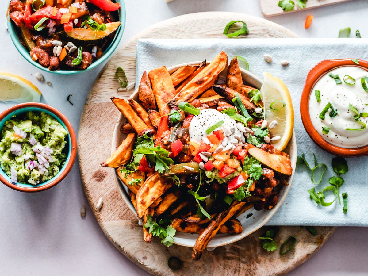 An overhead plate of roasted sweet potato with beans, salsa, guacamole and yogurt, with side bowls