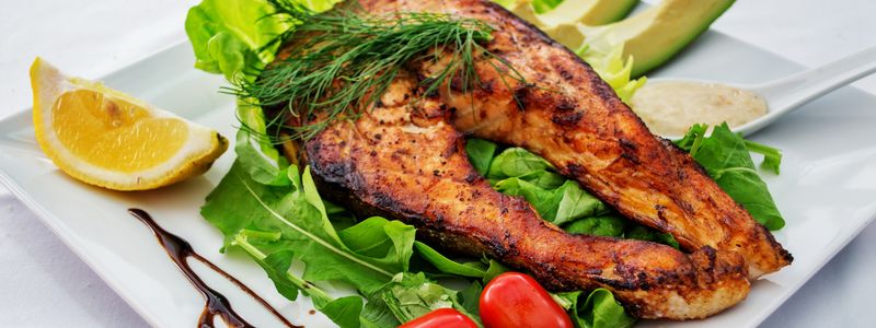 A cooked salmon fillet served on greens with lemon and tomatoes