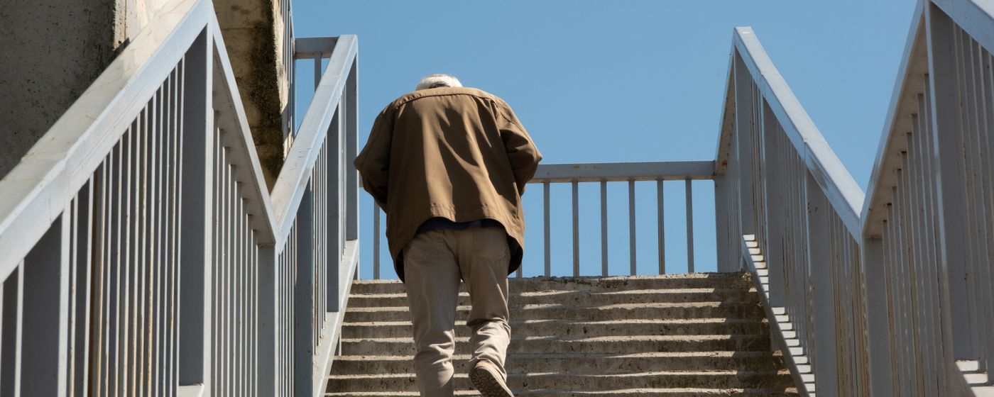 An older man climbing outdoor concrete stairs, seen from behind