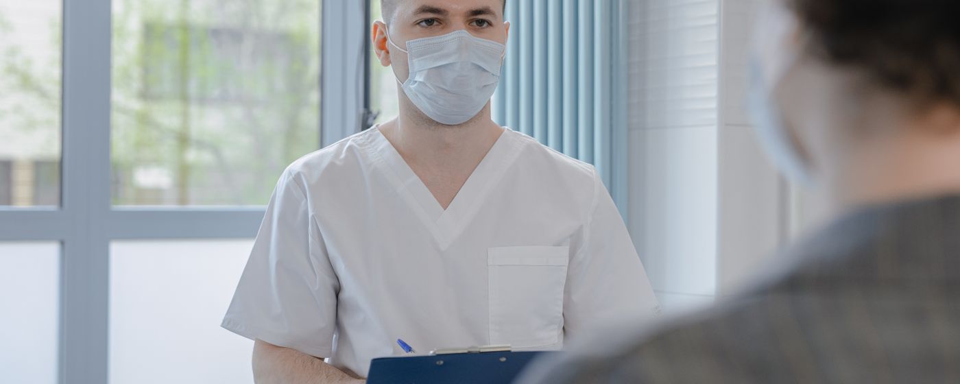 A medical professional in scrubs taking notes during a patient consultation