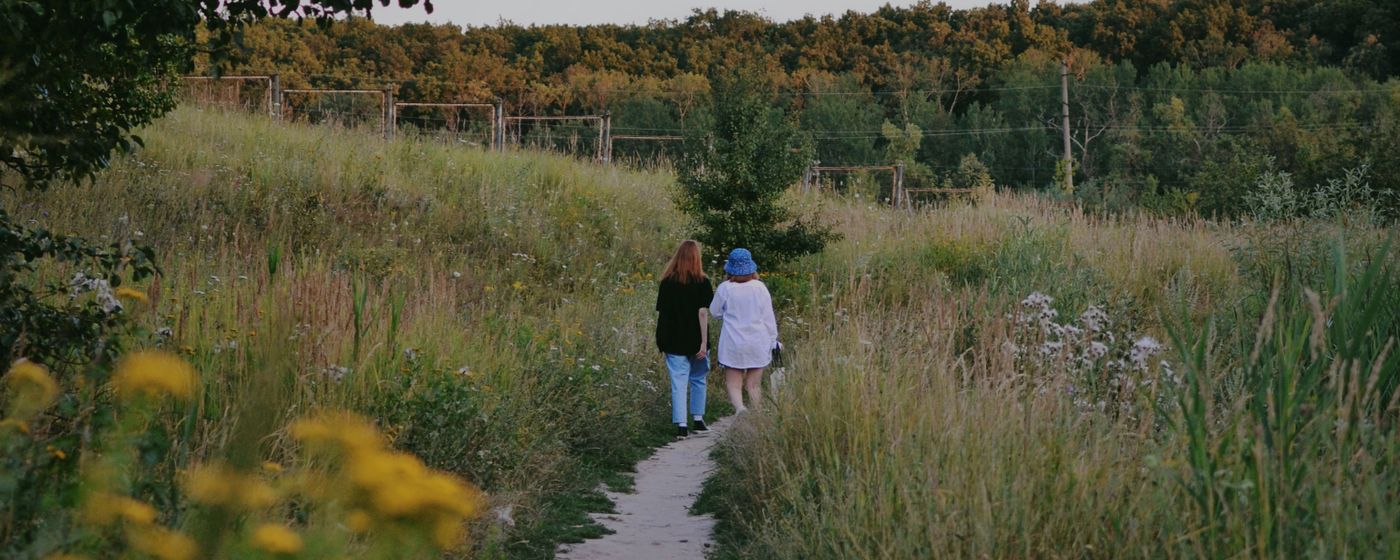 Two people walking on a narrow path between tall grass