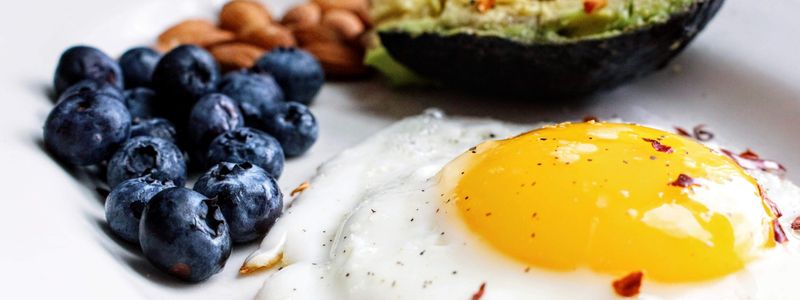 A breakfast plate with a fried egg, avocado, almonds and blueberries