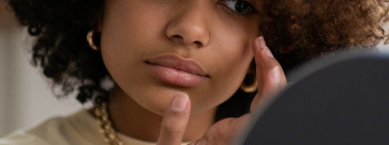 A woman looking closely at her skin in a hand mirror