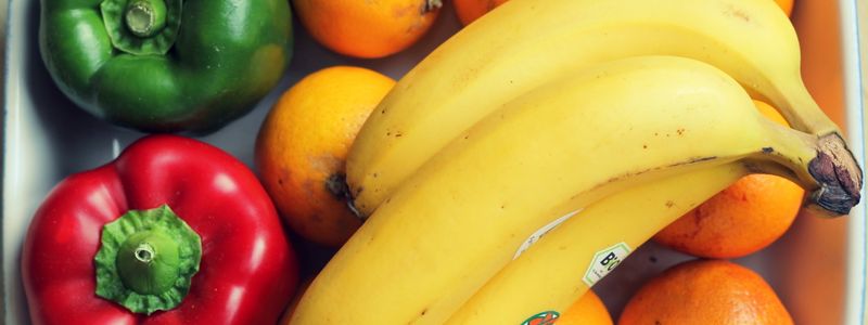 Bananas and oranges in a bin alongside bell peppers