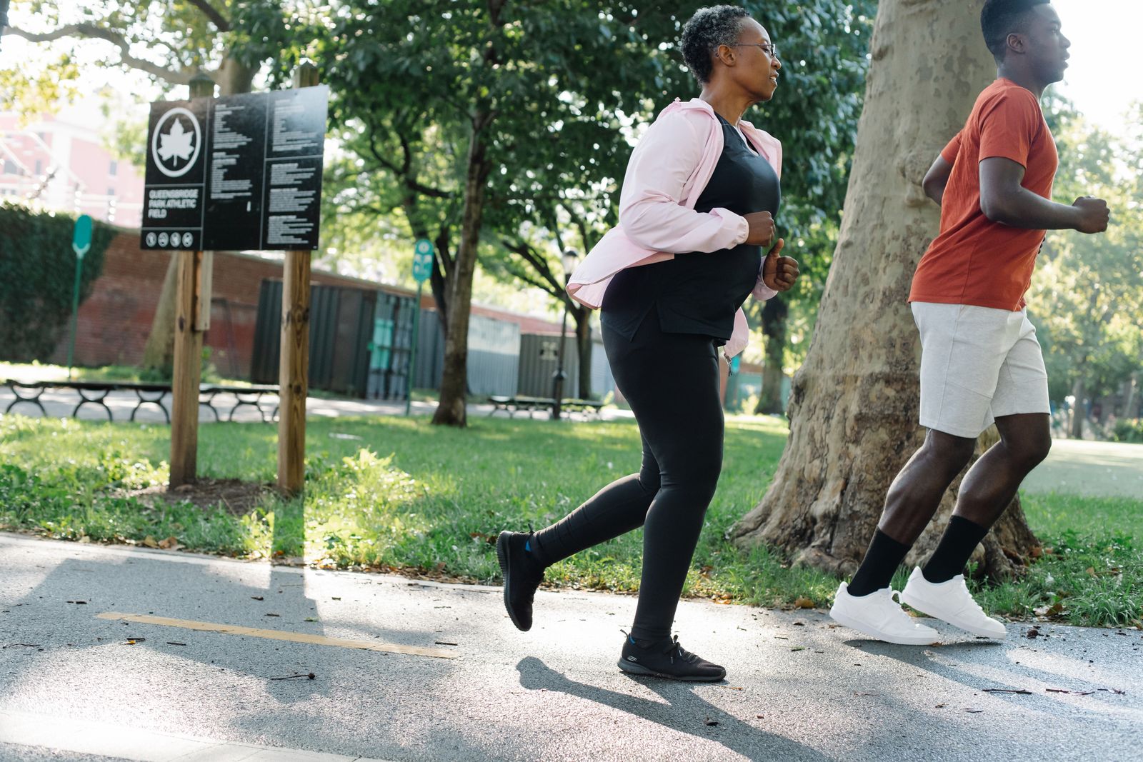 Two adults running together on a park path on a sunny morning