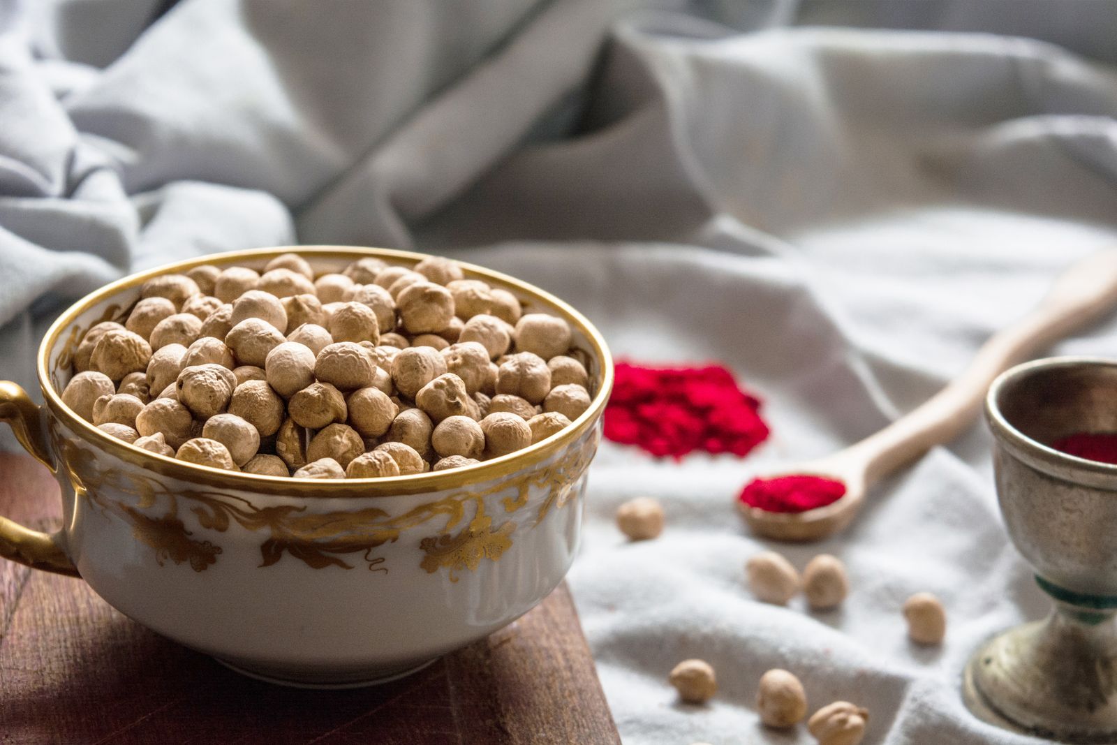 A bowl of dried chickpeas on a wooden board beside a cloth and a spoon of red spice