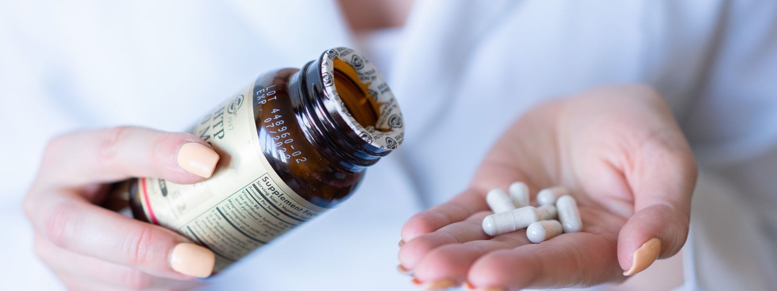 Hands tipping capsules from a supplement bottle into an open palm with the supplement facts panel visible