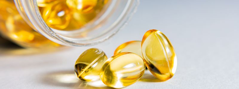 Golden softgel supplement capsules spilling from a small glass jar