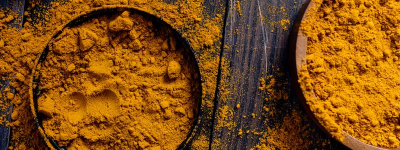 Bowls of bright golden turmeric powder on a dark wooden surface