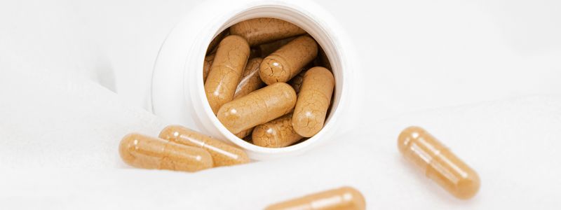 Tan herbal supplement capsules spilling from a white bottle