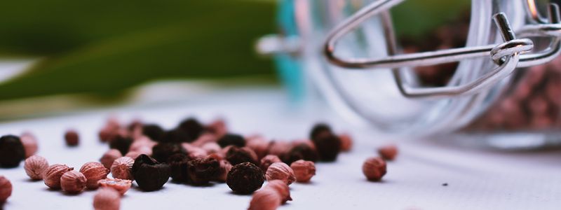 A scatter of black and pink peppercorns beside a glass jar