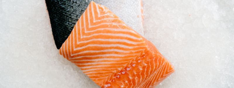 A fresh raw salmon fillet resting on ice, showing its marbled fat lines