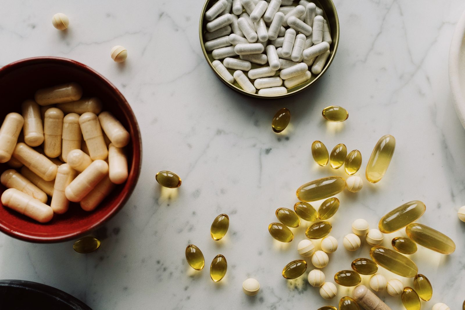 Capsules and softgels of several different sizes and colours spread across a marble surface