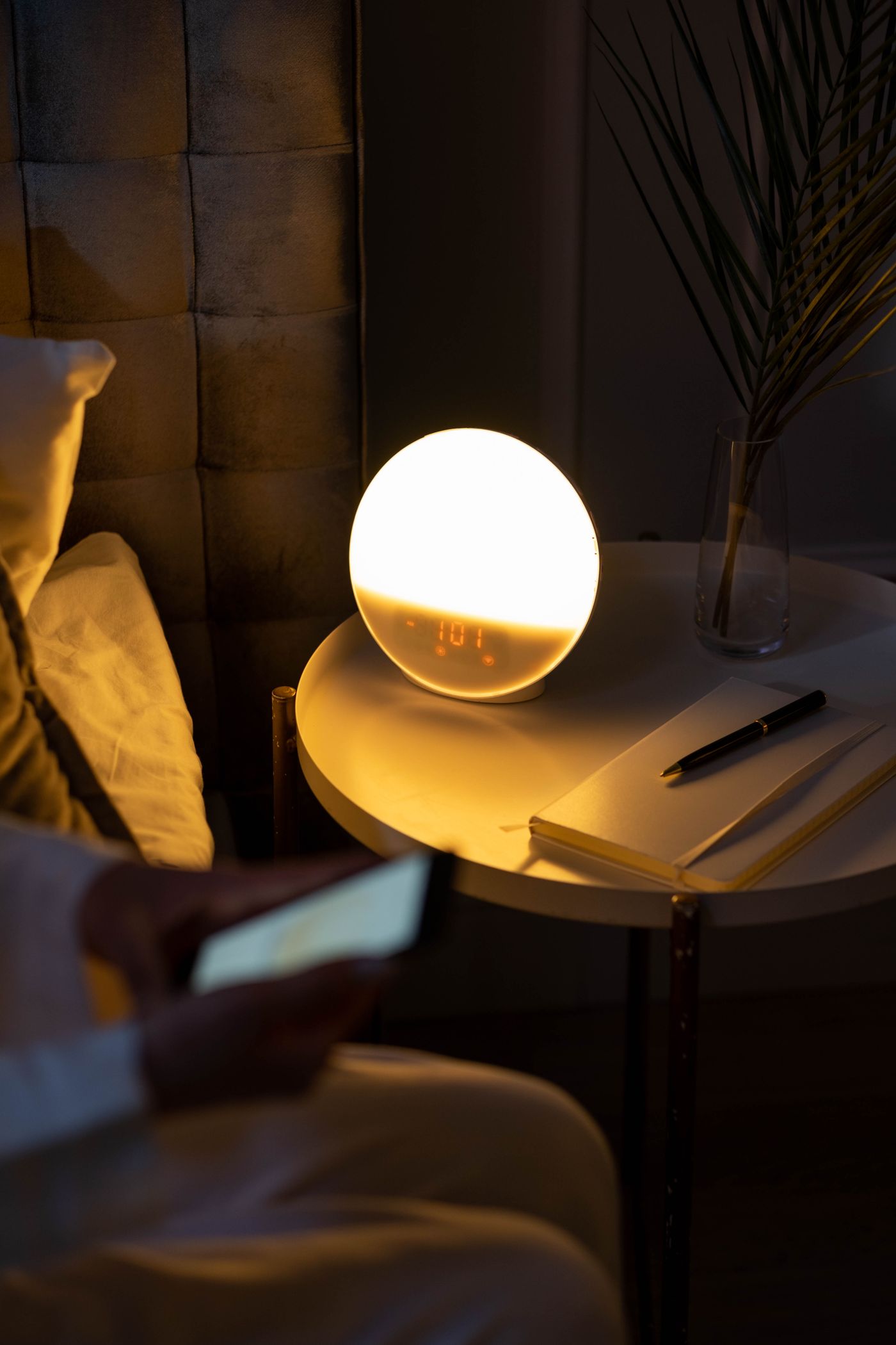 A dim bedroom at night with a lit clock reading past one in the morning and a phone screen glowing in bed