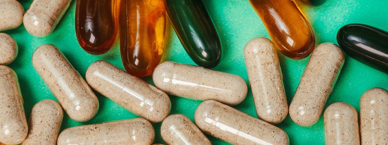A close-up of assorted supplement capsules on a green surface