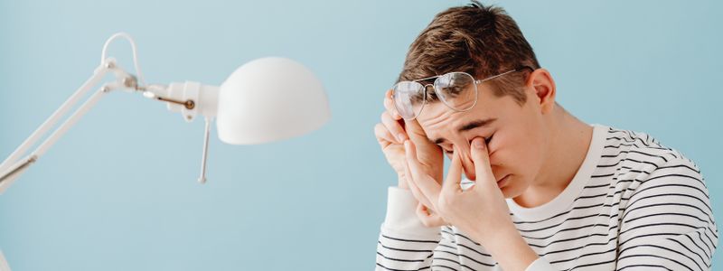 A person rubbing tired eyes with glasses pushed up on the forehead