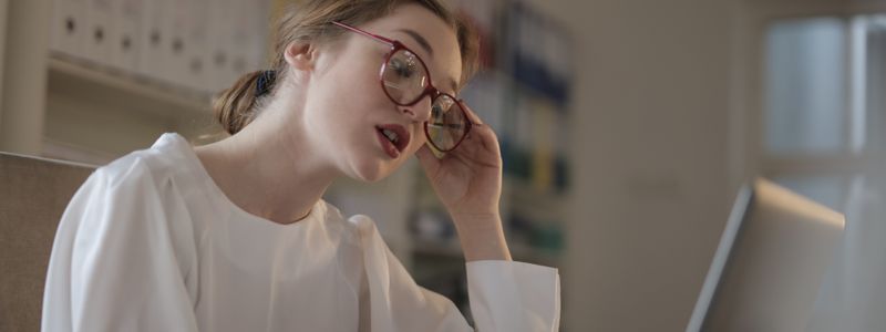 A woman in glasses focusing on a laptop screen in an office