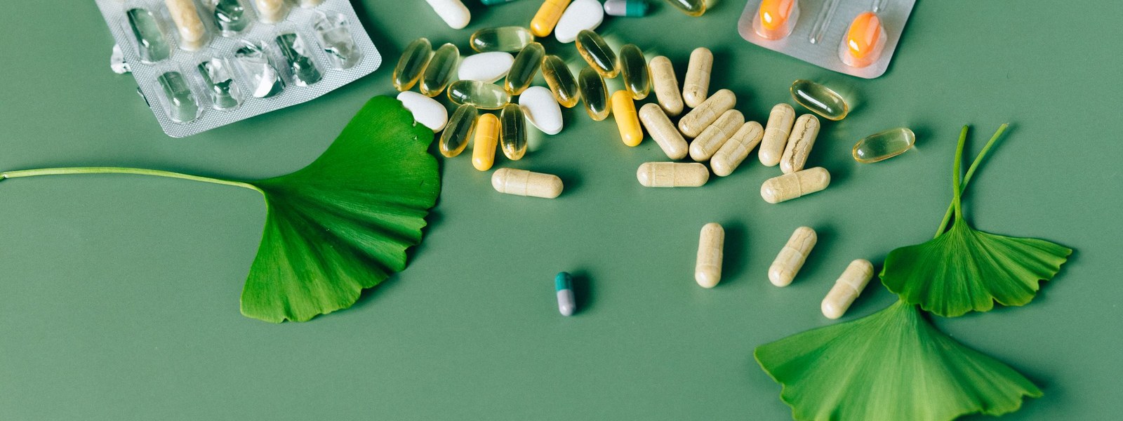 Assorted capsules, tablets and blister packs scattered across a green surface