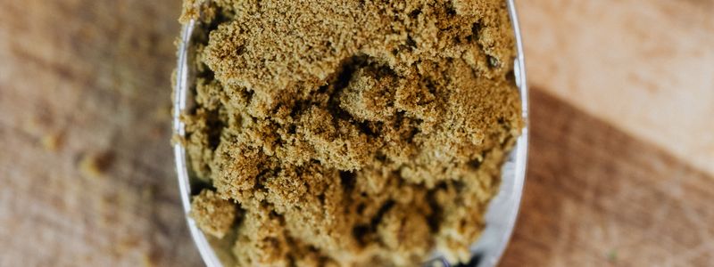 Brown shilajit-style powder in a metal scoop on a wooden surface