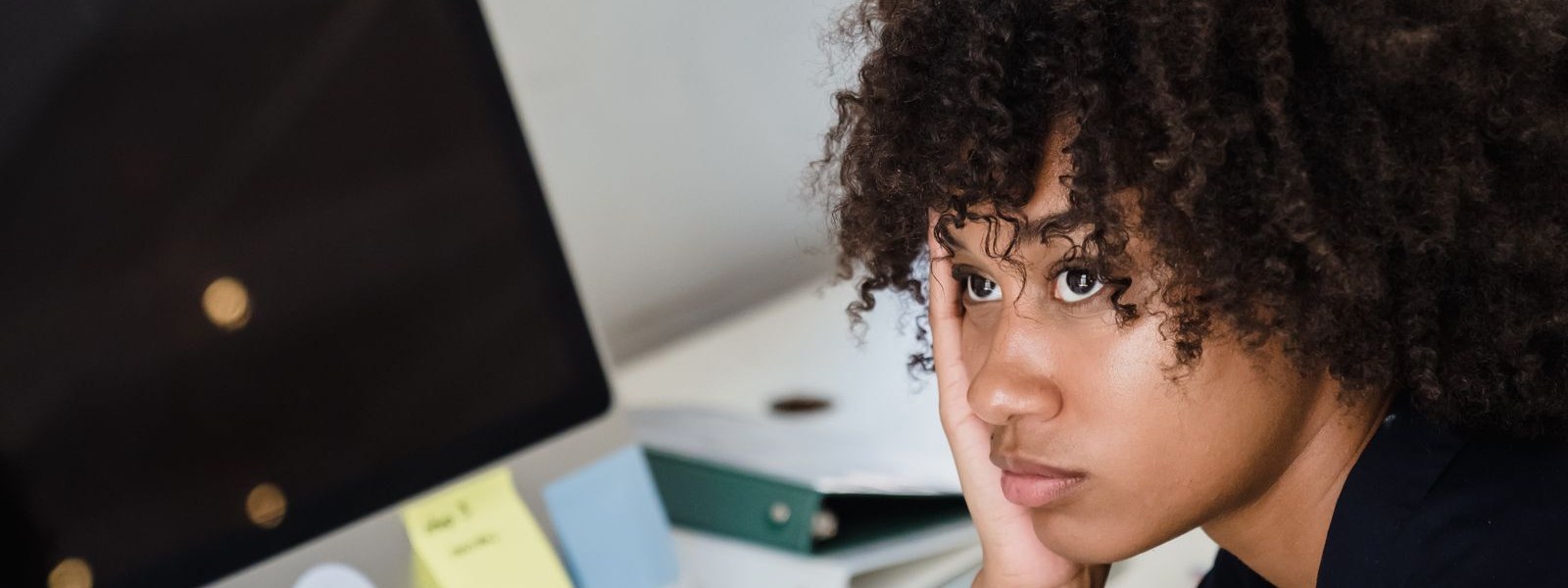 A person resting their head on one hand at a cluttered office desk