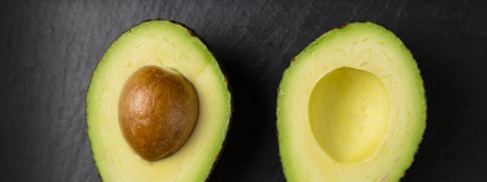 Two halves of a ripe avocado on a dark slate surface