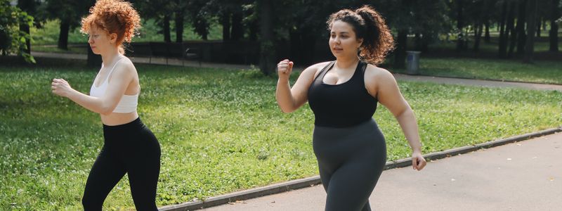Two women walking briskly along a park path with their arms bent, working up a moderate pace