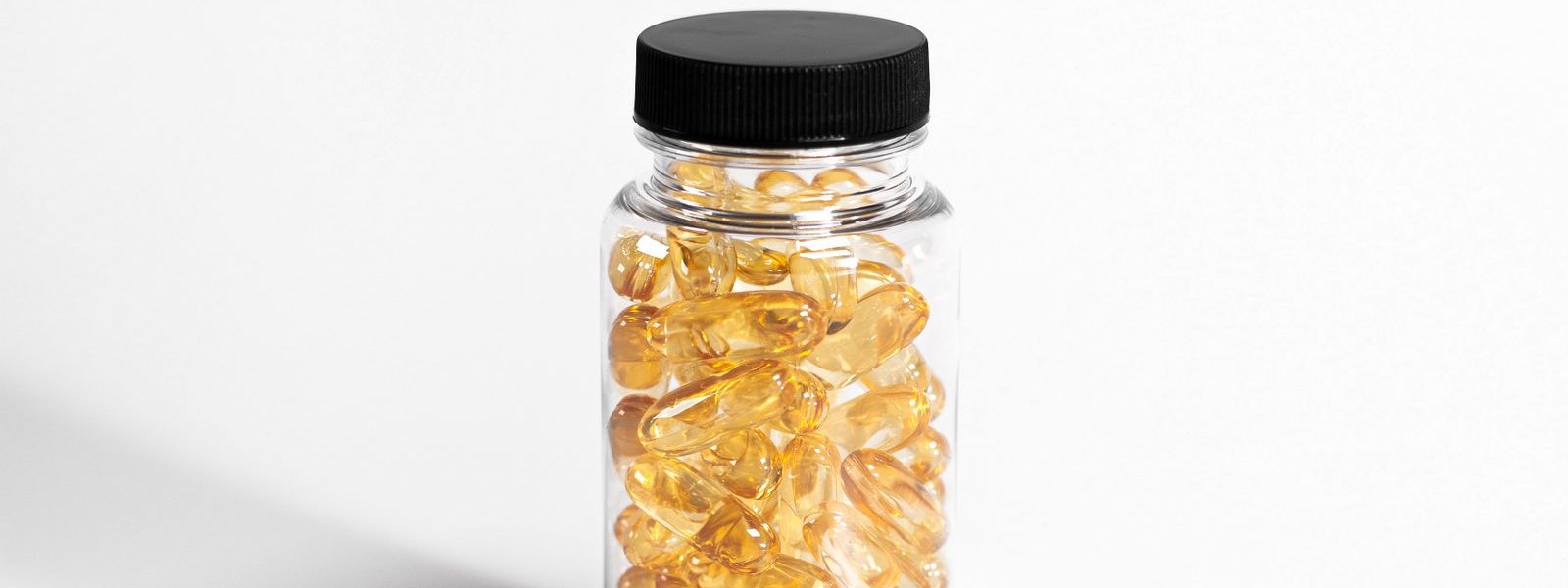 A clear bottle of golden softgel capsules on a white background