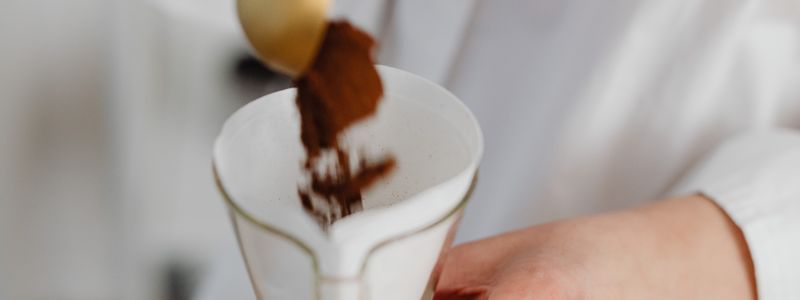 Dark brown powder being poured into a white vessel