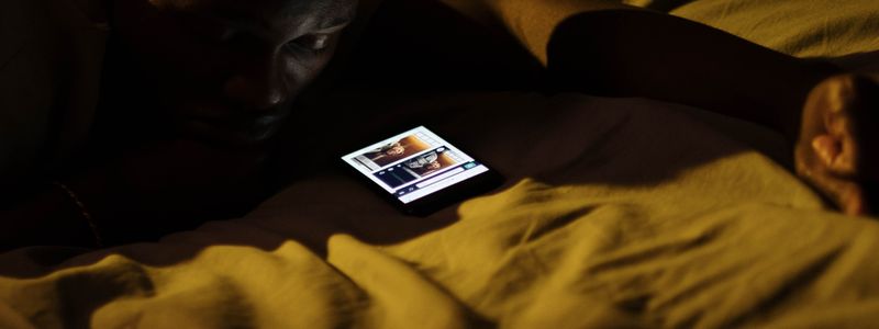 A person lying in bed at night looking at a glowing phone screen