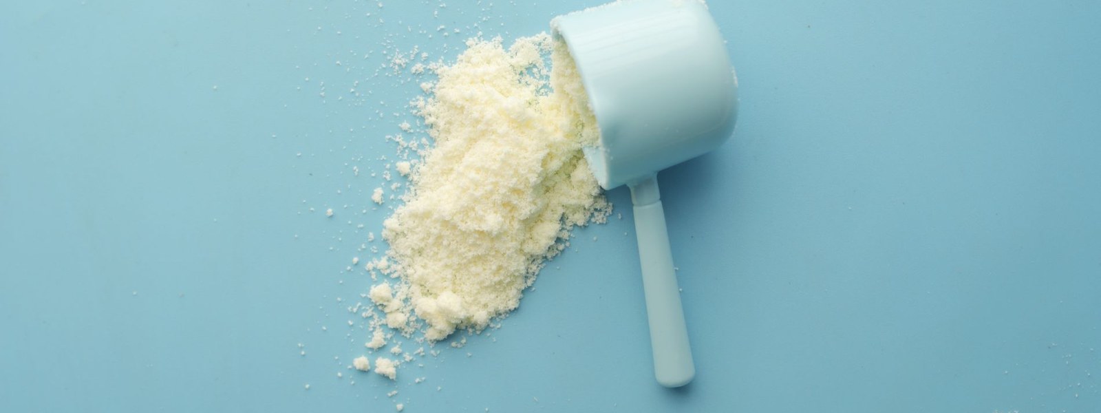 A measuring scoop tipped over with white powder spilling out on a blue surface