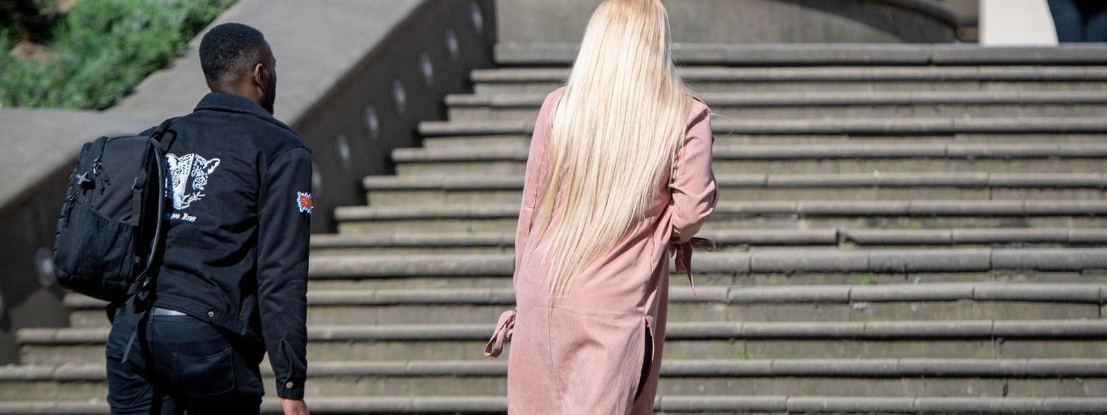 Two people walking up a wide flight of outdoor stone steps in daylight