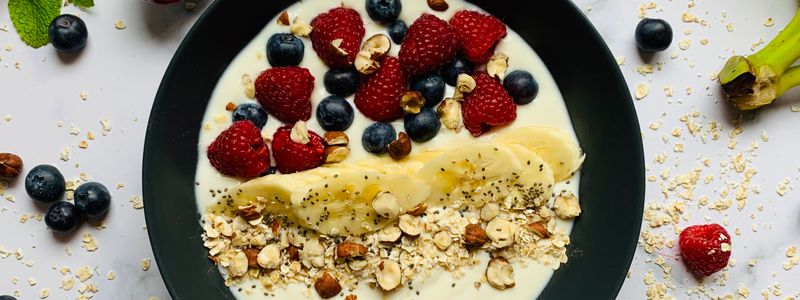 A bowl of oatmeal topped with berries, banana and nuts with loose oats scattered around