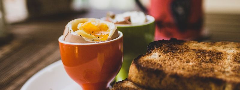 A soft-boiled egg in an egg cup beside slices of toast on a plate
