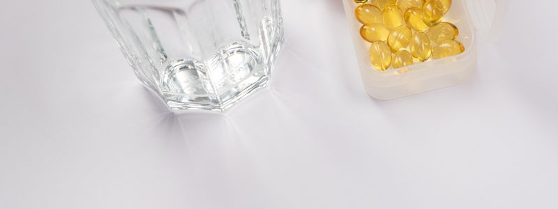 A hand reaching for a small case of golden capsules beside a glass of water