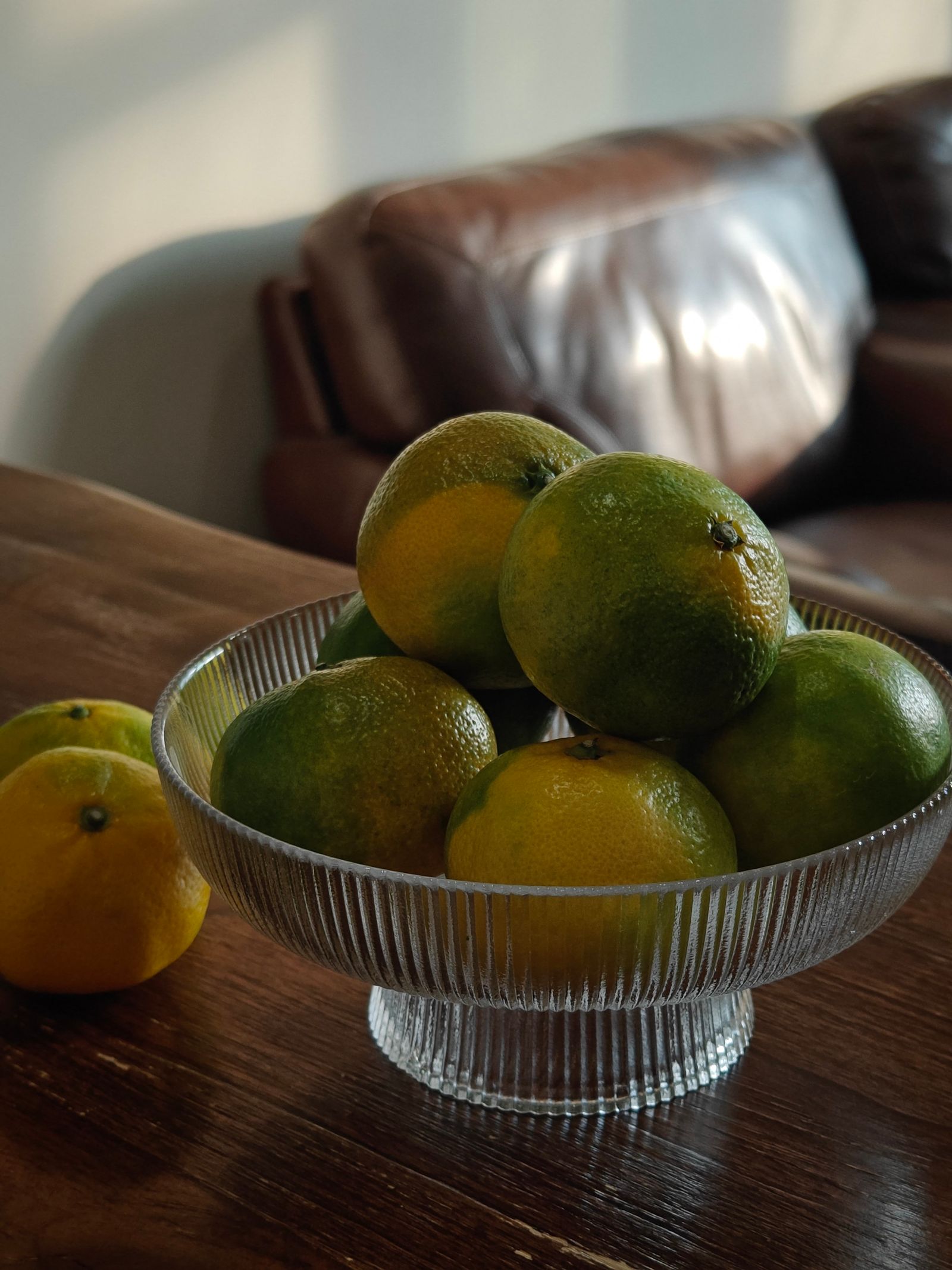 A glass bowl of fresh citrus fruit on a wooden table in a living room