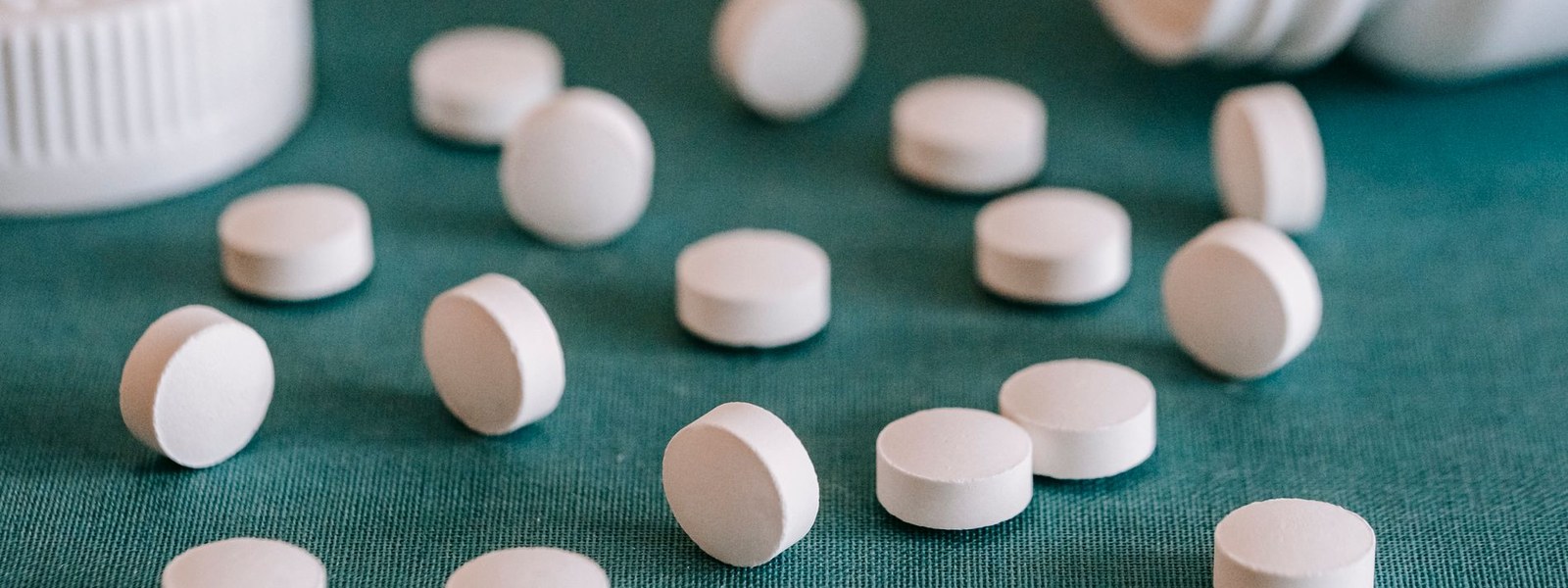 White supplement tablets spilled across a dark green cloth beside an open bottle
