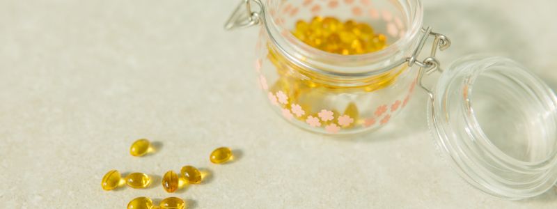 Golden capsules in a small glass jar with several spilled beside it