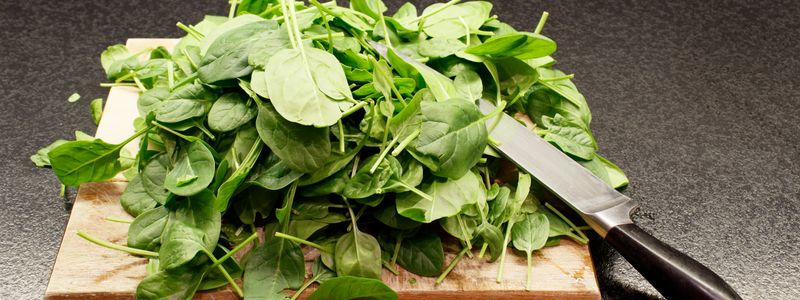 A pile of freshly chopped spinach and salad greens on a wooden cutting board with a knife