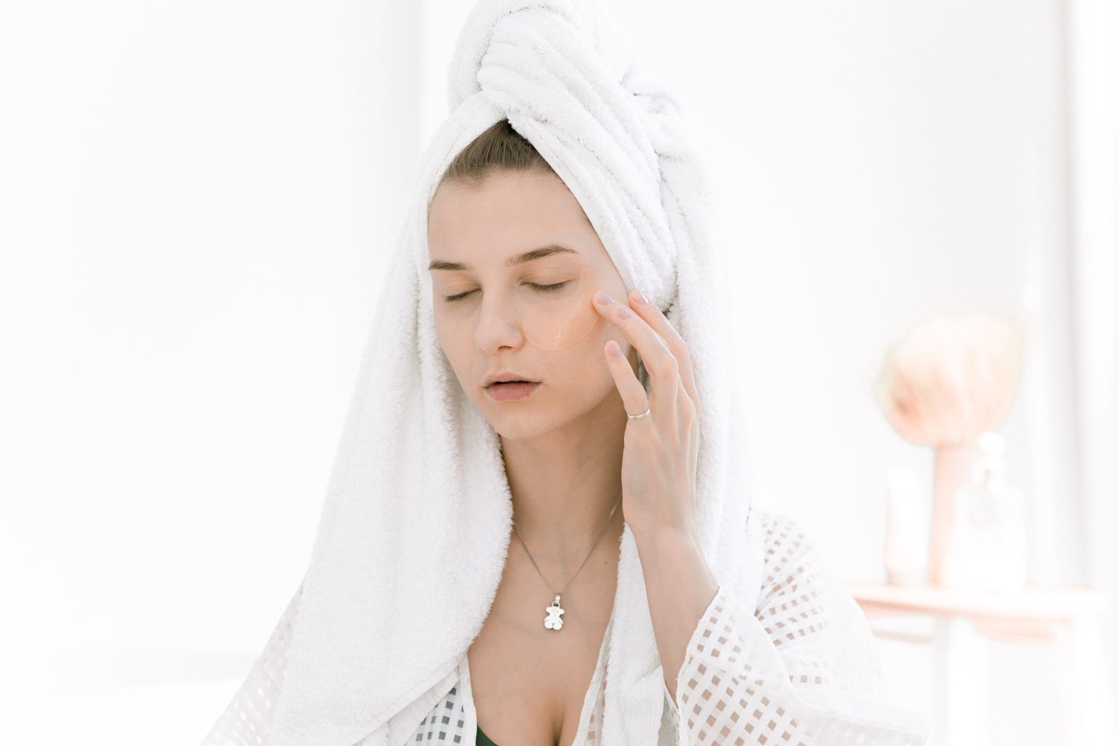A woman applying a moisturizer to her cheek in soft bright light