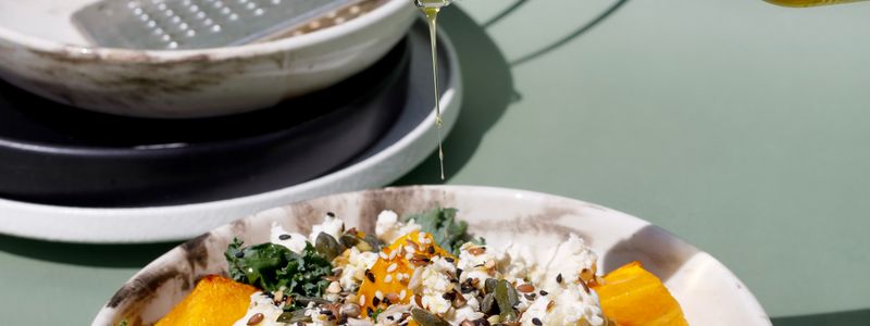 Olive oil being drizzled over a fresh grain and vegetable bowl