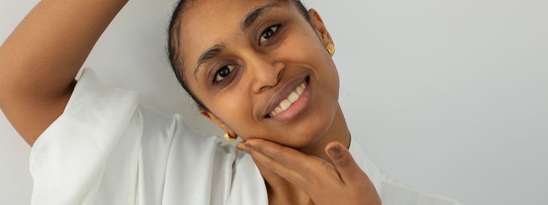 A smiling woman with healthy, clear skin resting her hand against her face