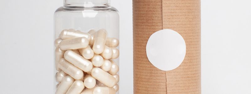 A clear supplement bottle of unlabeled cream-colored capsules beside a plain package