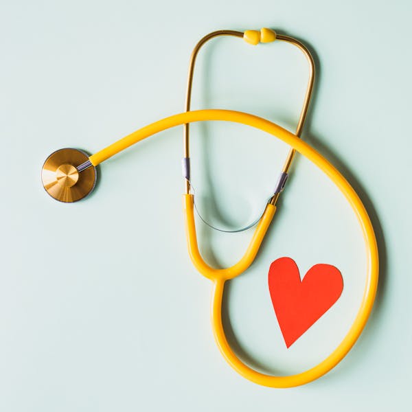 A stethoscope beside a paper heart on a pale background